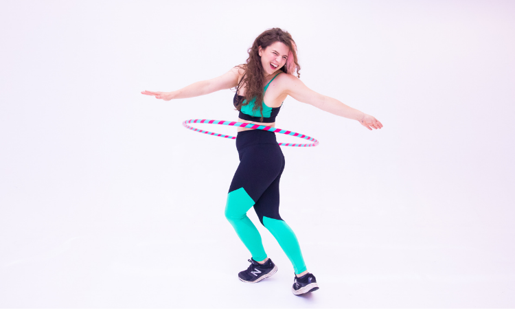 A photo of Daisy, a white woman with dark hair, looking joyous with a hoop spinning around her waist