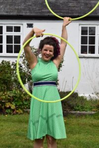 Daisy is outdoors with two yellow hoops in her hands wearing a green dress