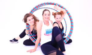 three hula hoopers smiling and sitting near a stack of hoops